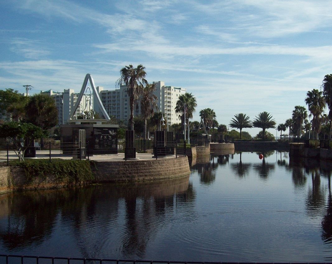 Lakefront cityscape with palm trees, white buildings, and reflections on calm water at sunset