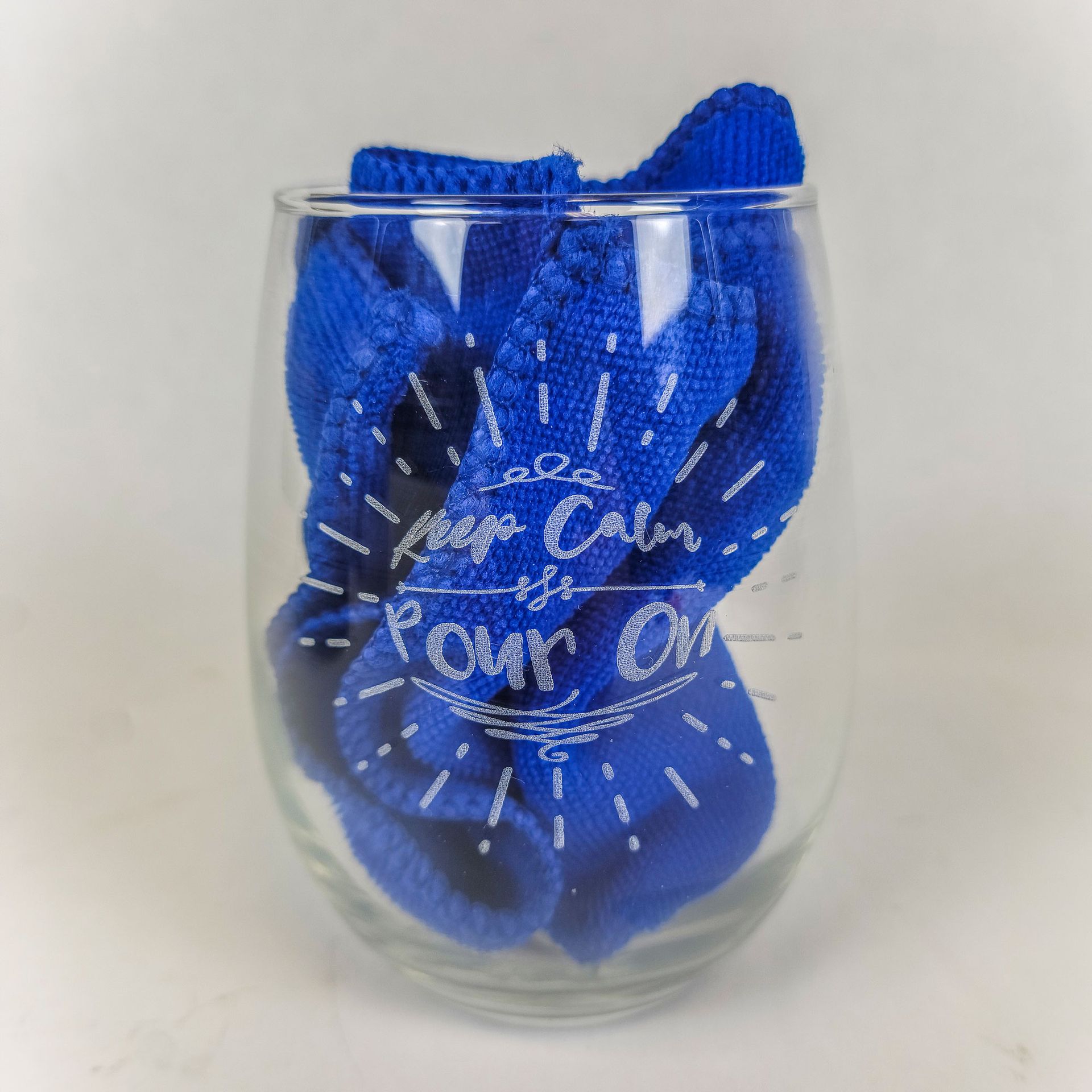 Stemless glass engraved with “Keep Calm Pour On” and filled with blue cloth.