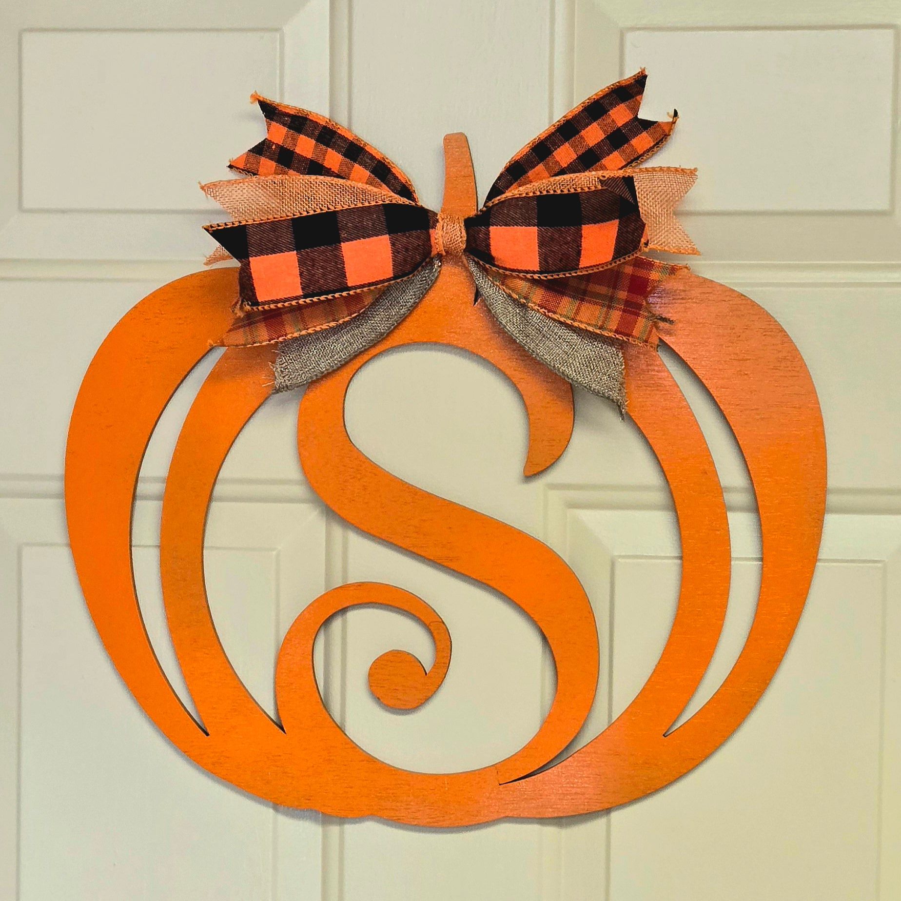 Orange pumpkin door hanger with monogram S and plaid bow.
