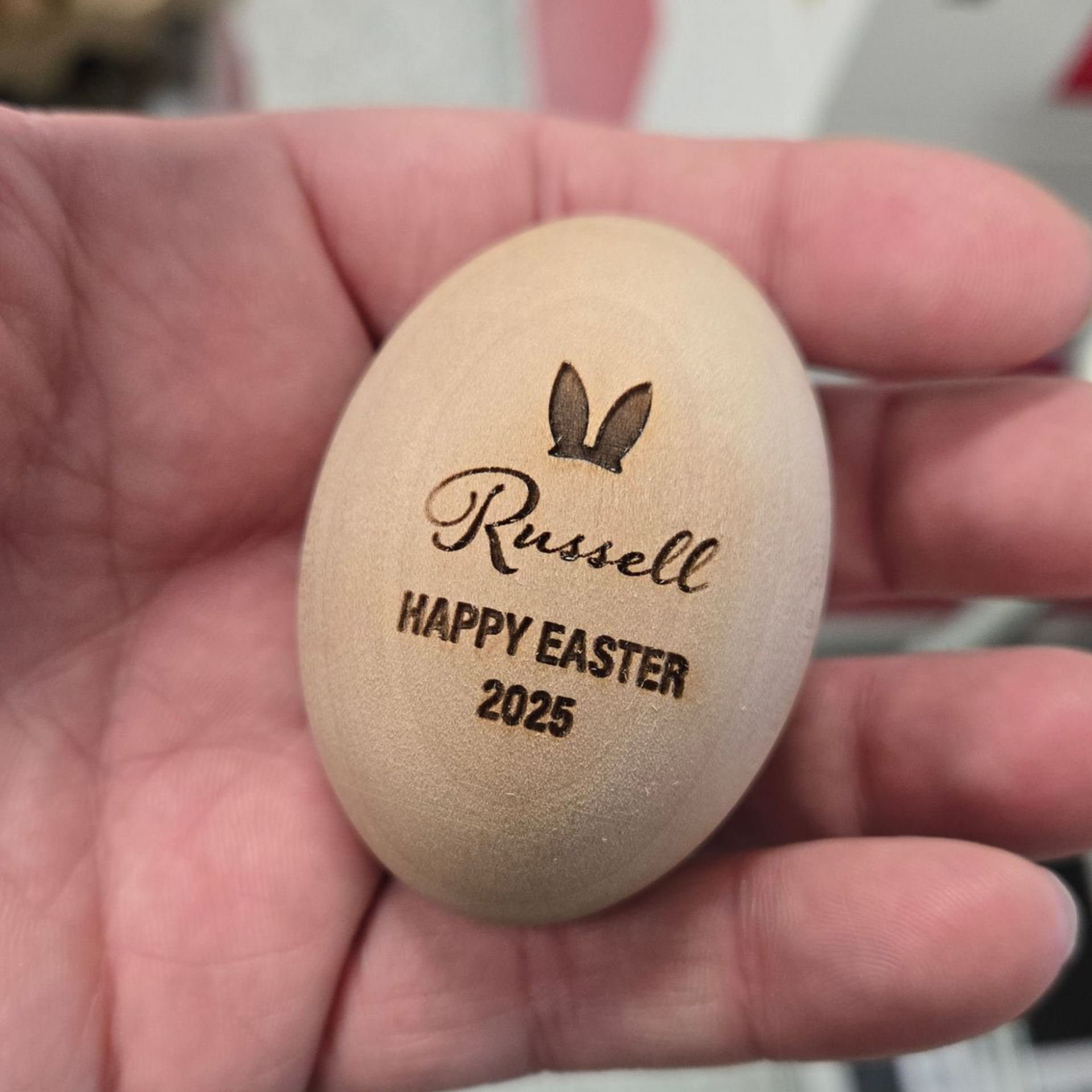 Engraved wooden Easter egg held in hand with personalized name and bunny design.