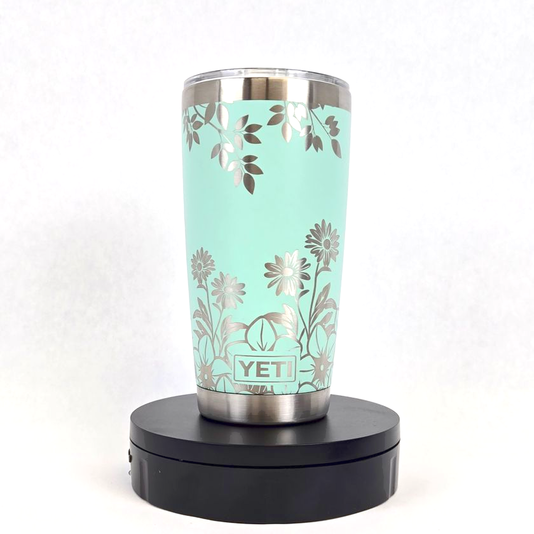 Mint green YETI tumbler engraved with floral design on a rotating display stand.