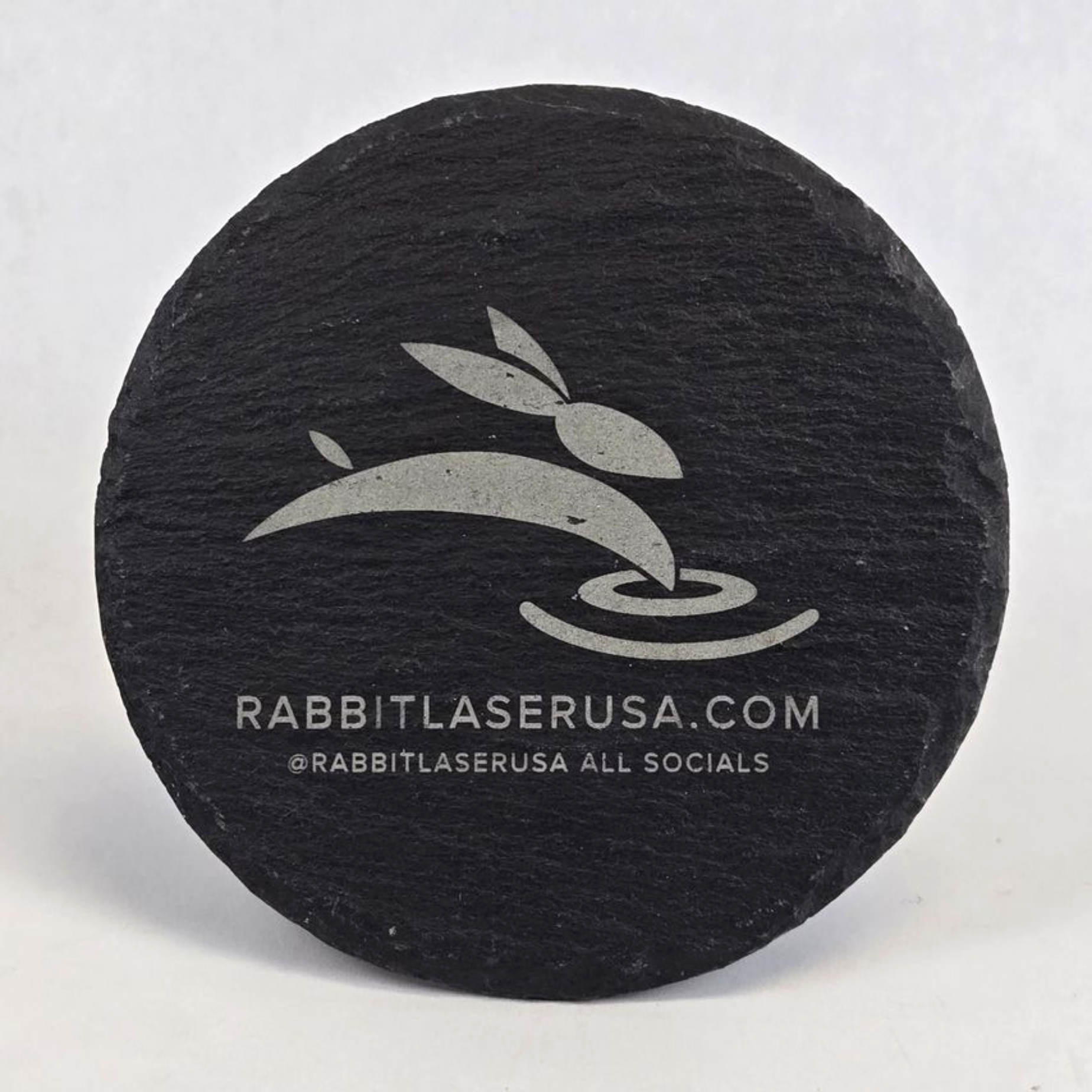 Round slate coaster engraved with Rabbit Laser USA logo and website information
