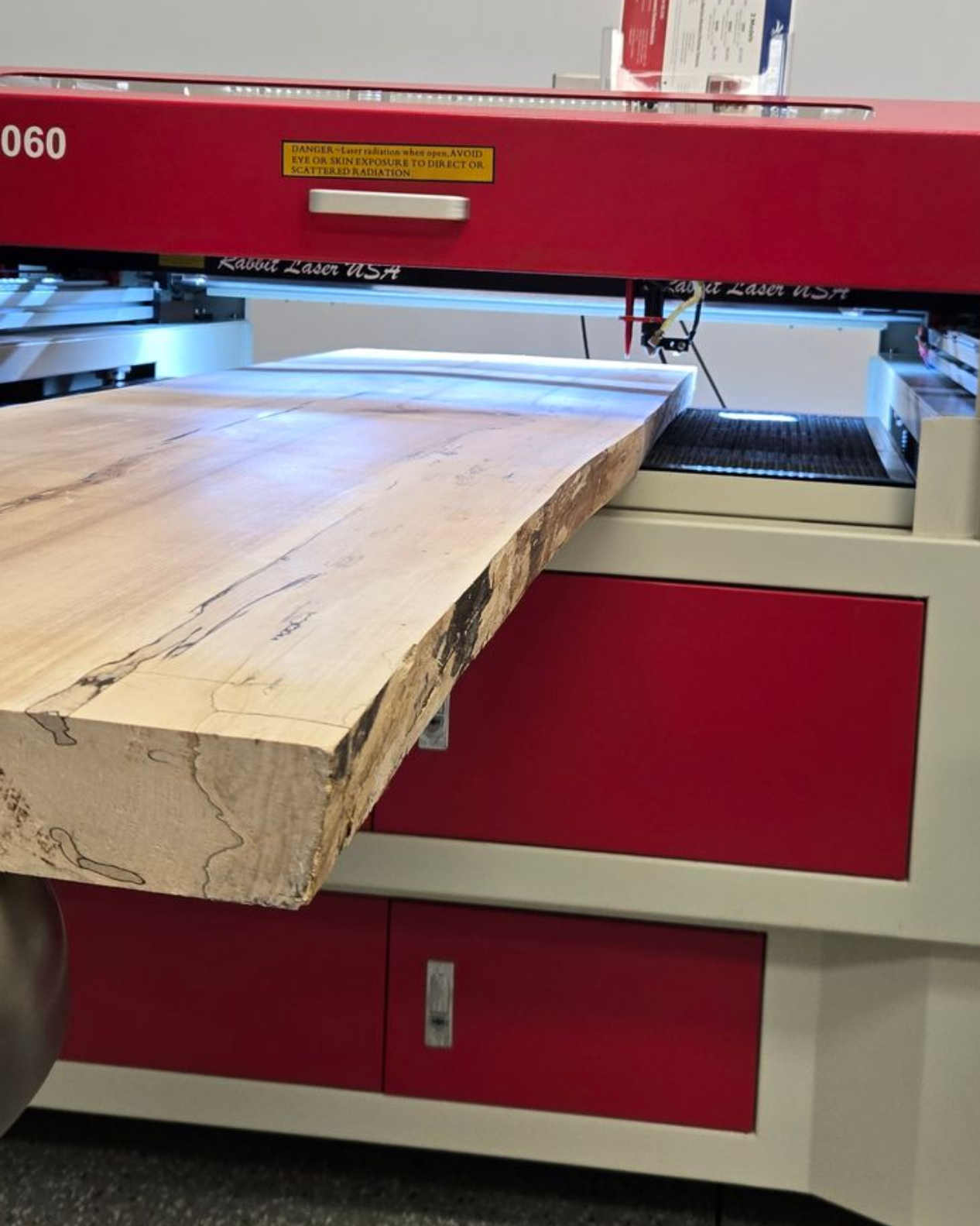 Live-edge wood bench back extending through an SD-60-9060 laser engraver during oversized project setup.
