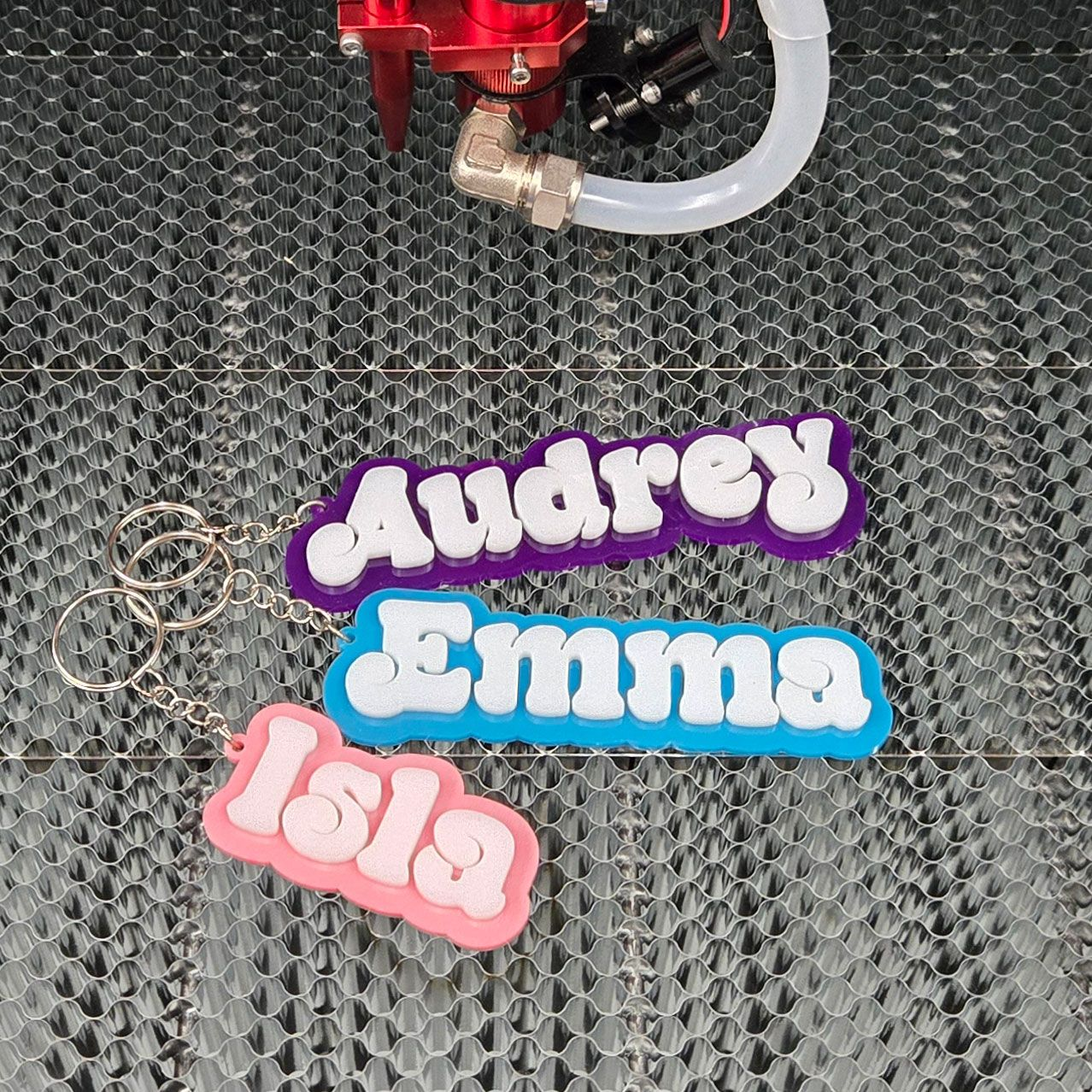 Colorful layered name keychains displayed on laser cutting bed with key rings
