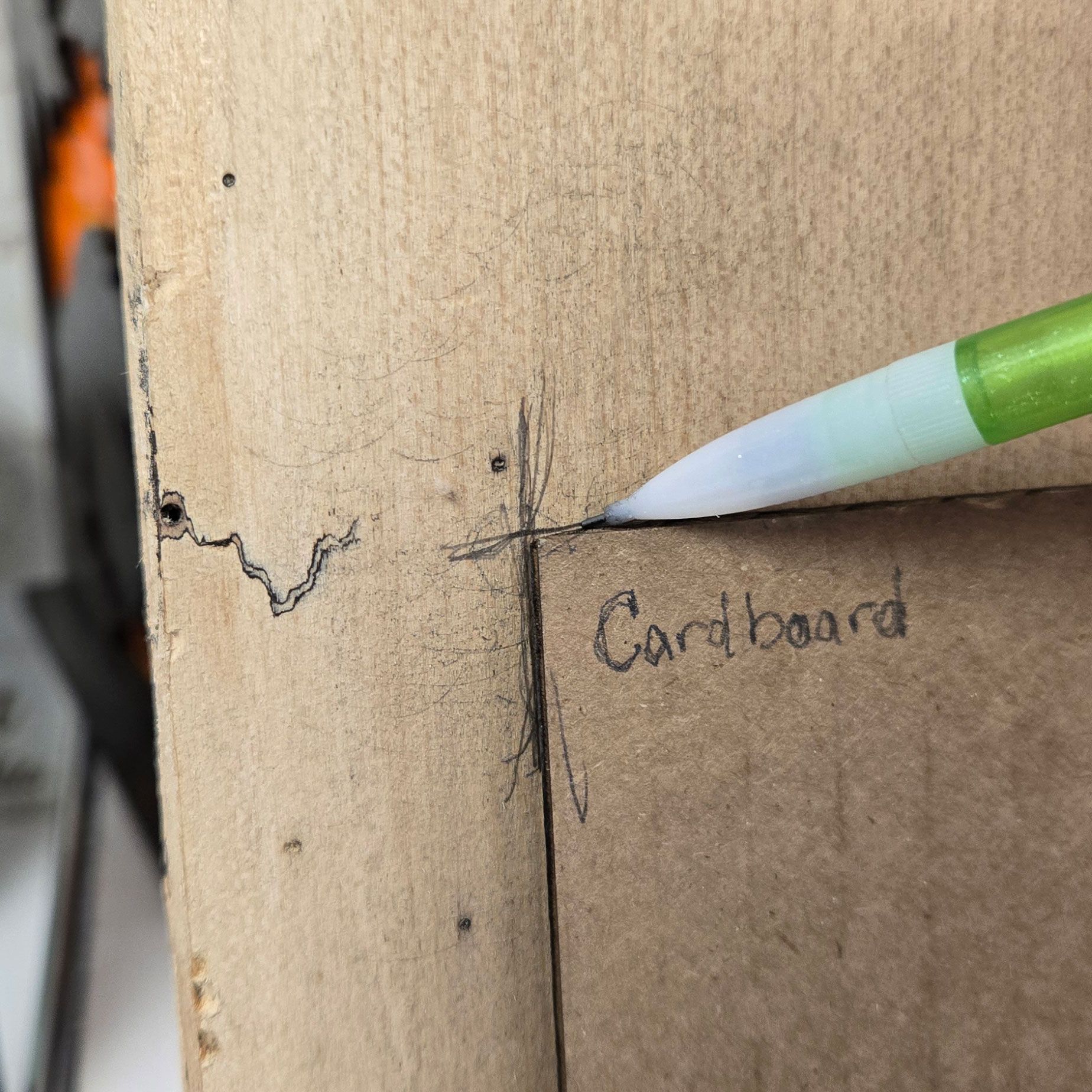 Cardboard corner template aligned on the wood while a pencil marks registration points for engraving.
