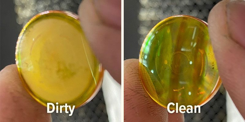 Side-by-side comparison of a dirty laser lens and a clean laser lens held by hand.