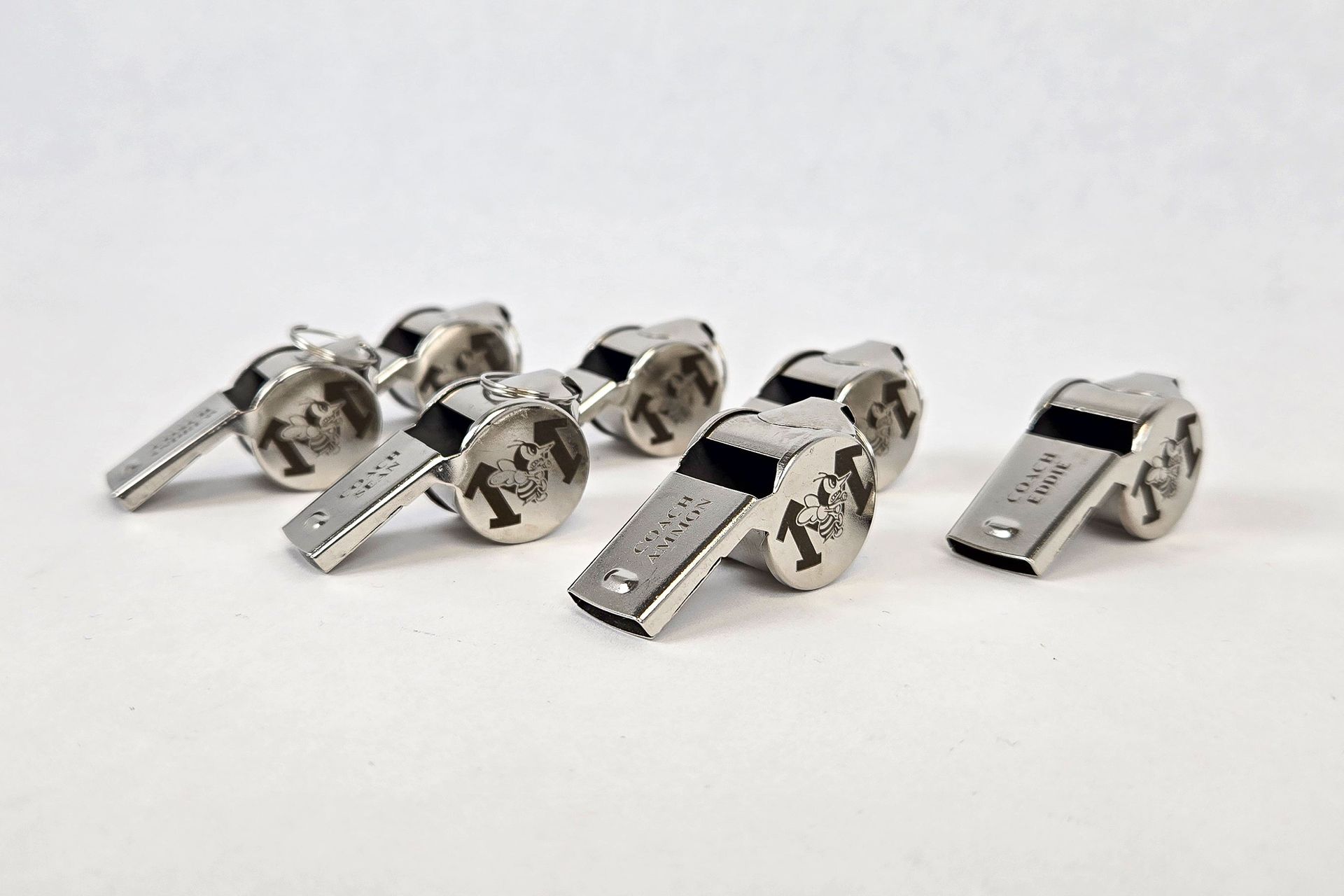 Laser engraved metal coach whistles with custom logo on white background
