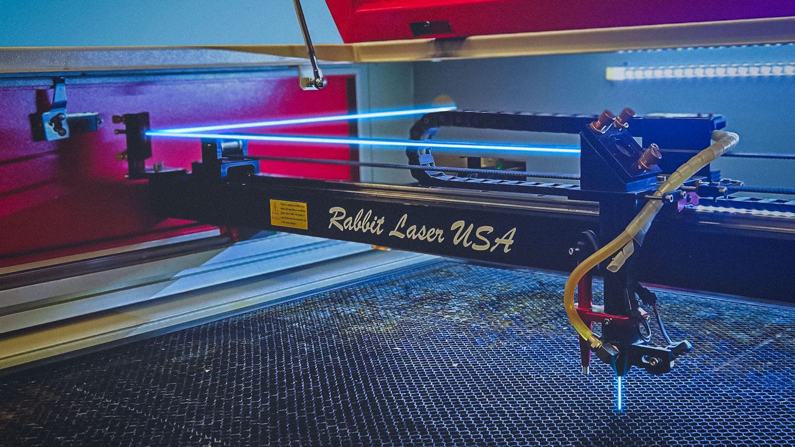 Interior view of a Rabbit Laser USA CO₂ laser machine showing the laser head and alignment mirrors, with blue guide lines illustrating the beam path used during mirror alignment.