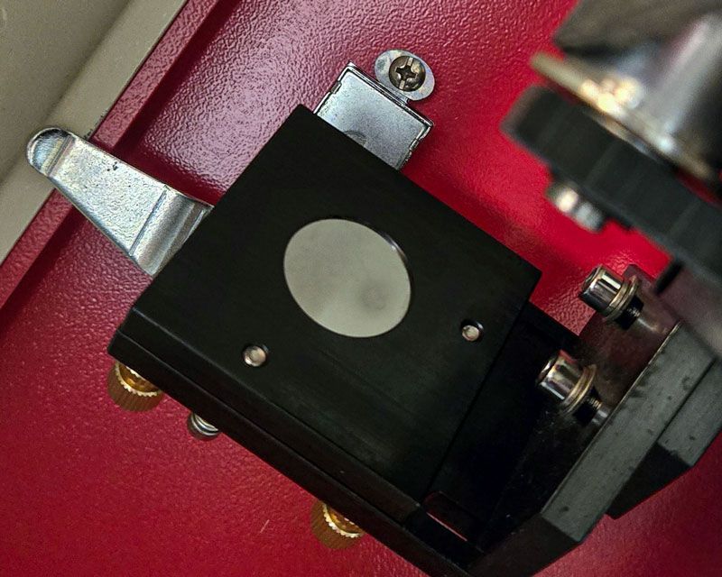 Close-up of a CO2 laser mirror being inspected for dust, residue, and buildup before returning the machine to use.