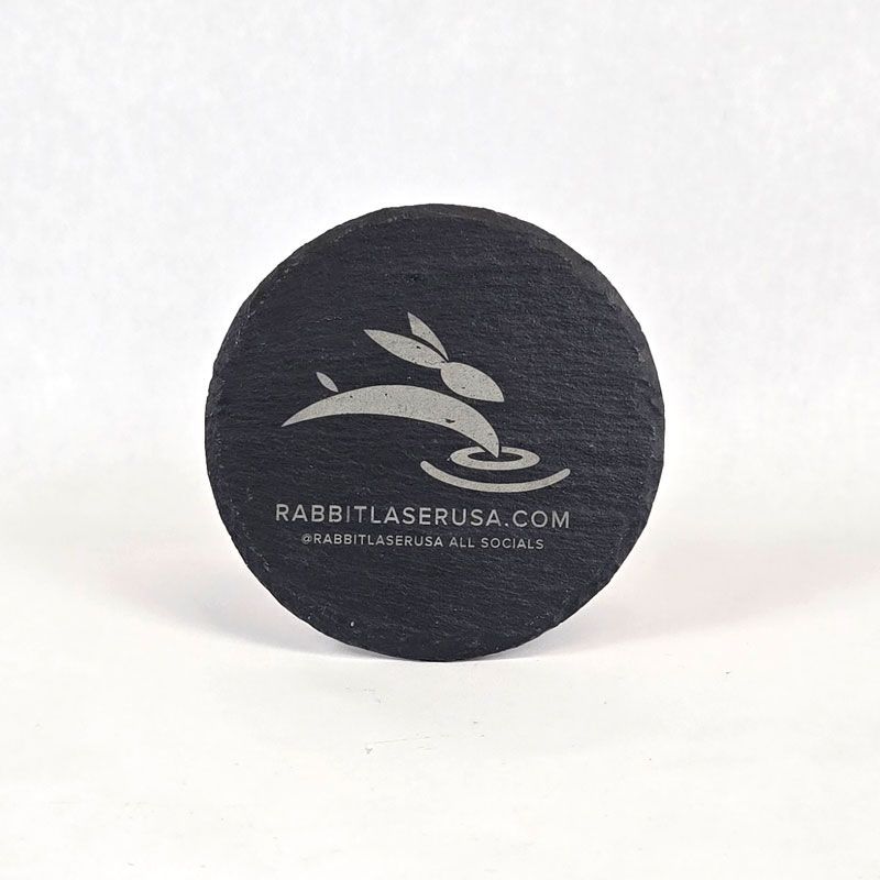 Black round slate coaster engraved with Rabbit Laser USA logo and website.
