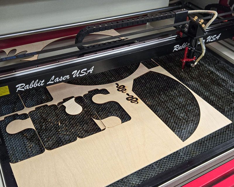 CO2 laser workbed with leftover plywood and cut scraps that should be cleared before restarting the machine.