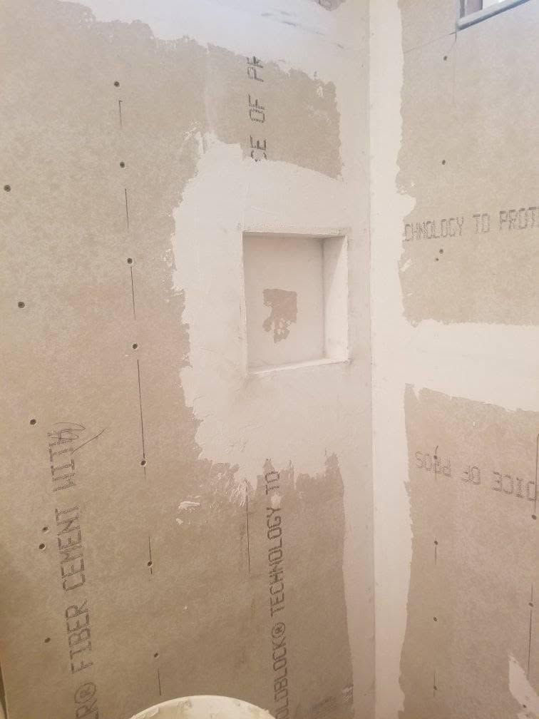 Unfinished bathroom wall with drywall patches and a small recessed niche.