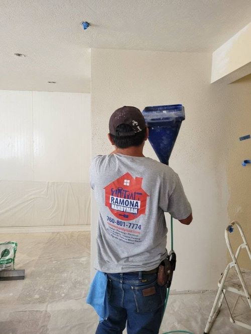 Worker applying texture to a wall with a blue hopper in a room under renovation