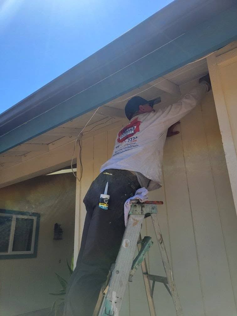 Person on a ladder painting the eaves of a house outdoors.