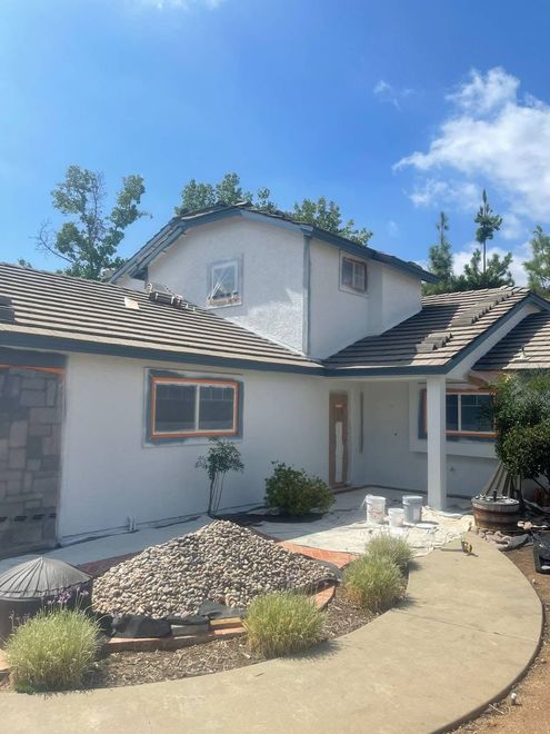 Modern two-story house with white stucco, gray roof, desert landscaping, and a curved walkway under a blue sky