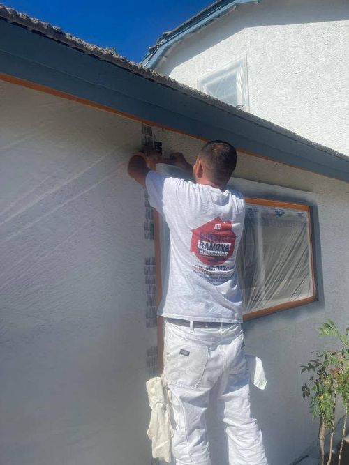 Person painting the exterior trim of a house under a blue roof eave