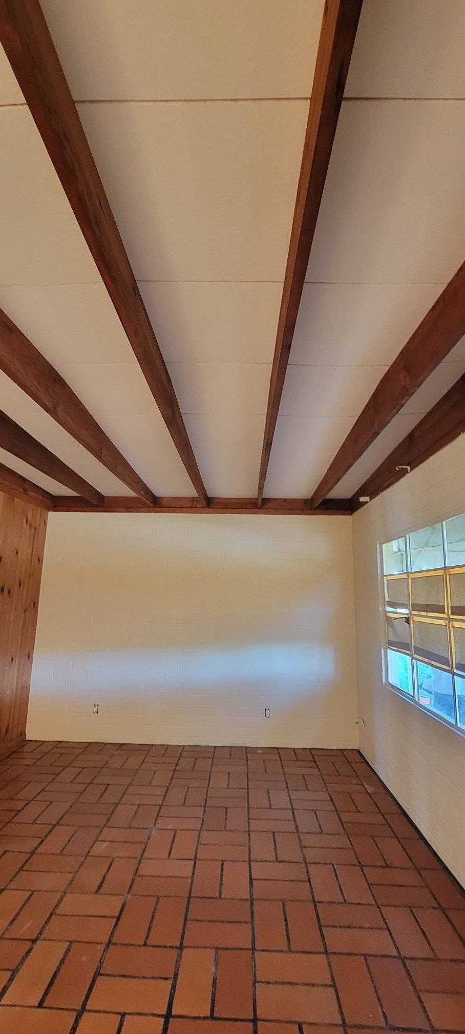 Empty room with terracotta tile floor, cream walls, and exposed wooden ceiling beams