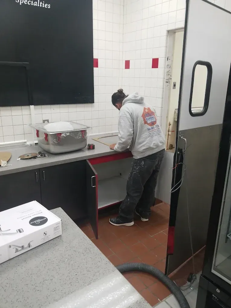 Worker in white jacket cleaning a sink in a commercial kitchen