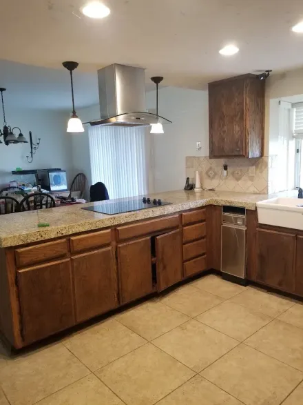 Kitchen with dark wood cabinets, tan tile floor, granite island, and stainless steel range hood.