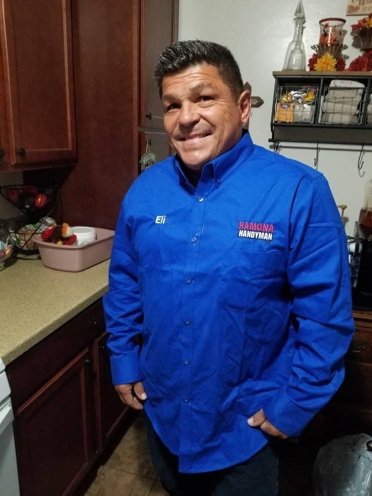 Man smiling in a kitchen, wearing a bright blue chef-style jacket.