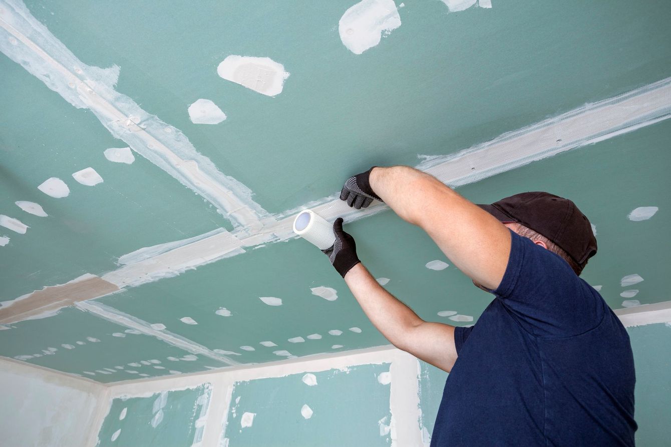 Un operaio leviga il soffitto in cartongesso con una levigatrice elettrica in una stanza in fase di ristrutturazione.