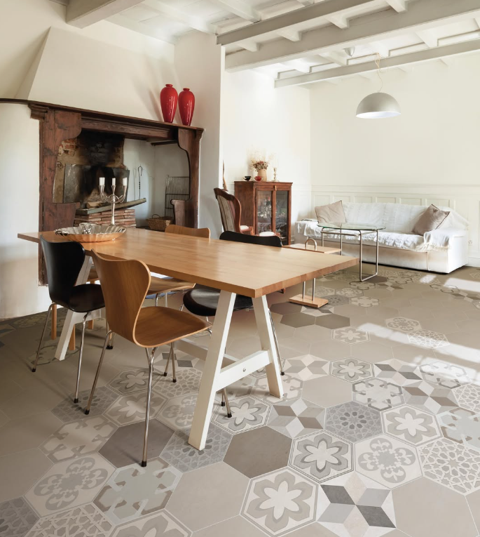 Luminosa sala da pranzo con tavolo in legno, sedie di diverse forme e dimensioni, divano bianco e pavimento piastrellato con motivi decorativi.