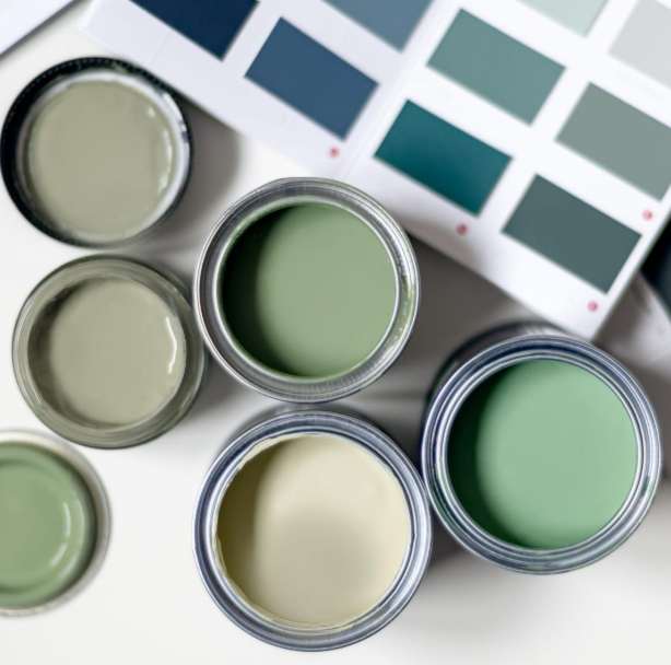 Barattoli di vernice aperti nei toni tenui del verde e del crema accanto a campioni di colore.