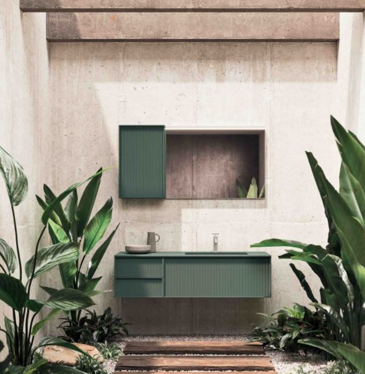 Zona lavabo esterna minimalista con mobili verdi, specchio e rigogliose piante tropicali.