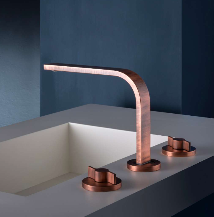 Rubinetto moderno in rame sopra un lavabo minimalista con due manopole abbinate su un piano blu scuro