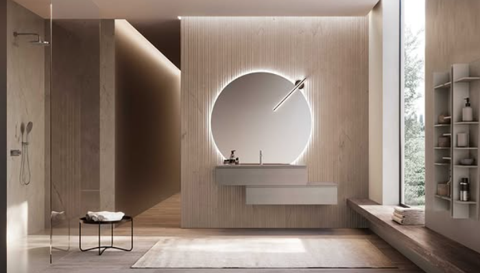 Bagno moderno e minimalista con specchio rotondo retroilluminato, mobile lavabo sospeso e tonalità beige neutre.