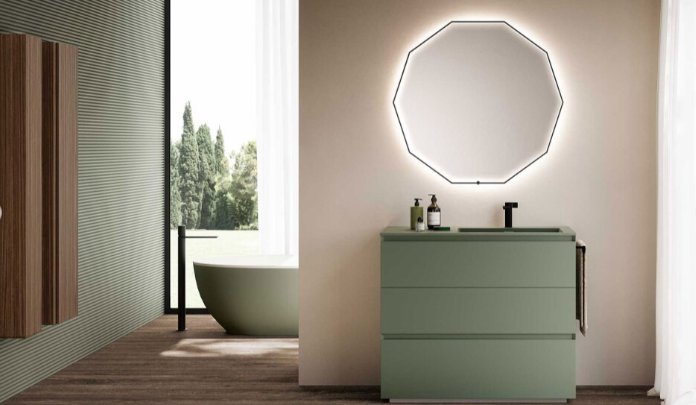 Bagno moderno con mobile lavabo verde, specchio ottagonale e vasca da bagno accanto a una finestra con vista sugli alberi.