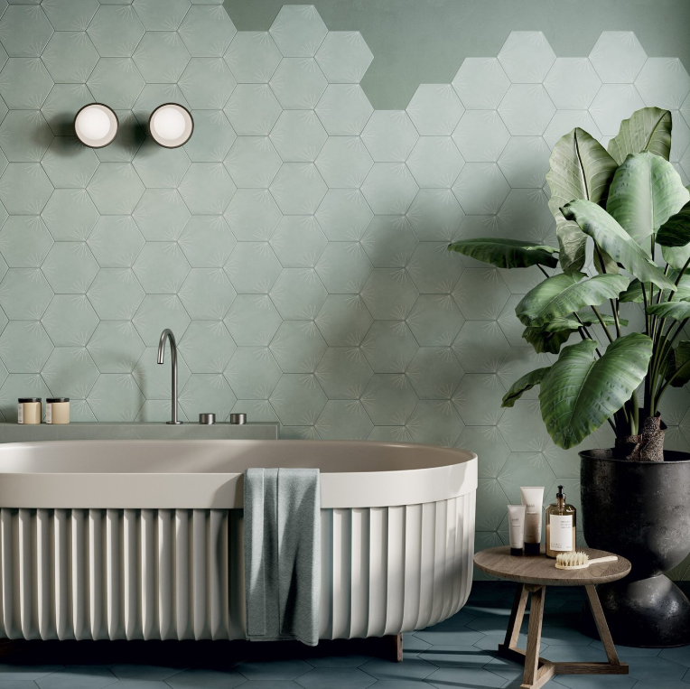 Bagno moderno con piastrelle esagonali color menta, vasca freestanding e pianta in vaso accanto a un piccolo sgabello.