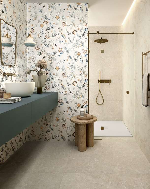 Bagno con carta da parati floreale, mobiletto color verde acqua, specchio rotondo, lavabo in pietra e cabina doccia in vetro.