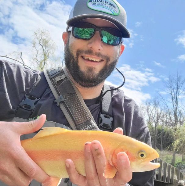 K's Outfitter owner David holding a golden fish outdoors under a blue sky