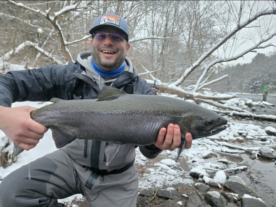 K's Outfitter owner David holding a large fish in a snowy stream with bare trees in the background