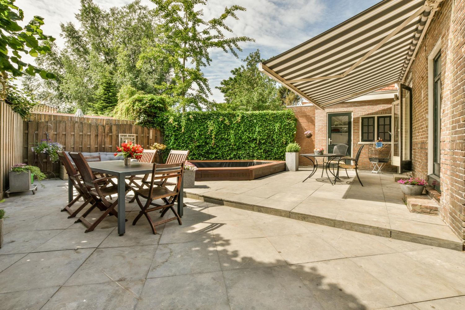Patio with dining set, striped awning, and lush green wall.