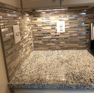 Kitchen countertop with granite, mosaic backsplash, and outlets under overhead lighting.
