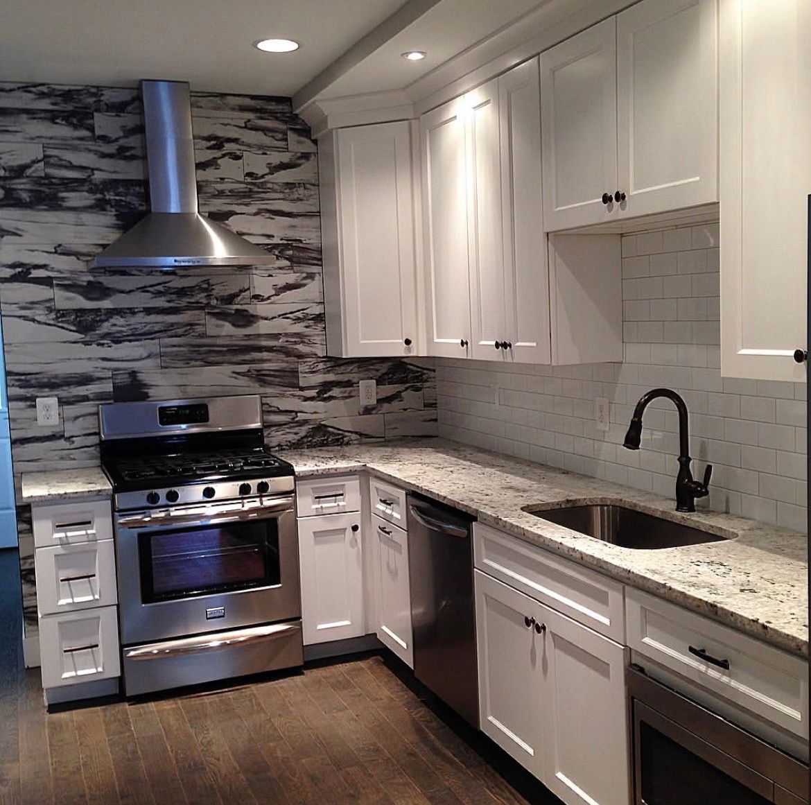 Kitchen with white cabinets, stainless steel appliances, stone backsplash, and dark wood floor.