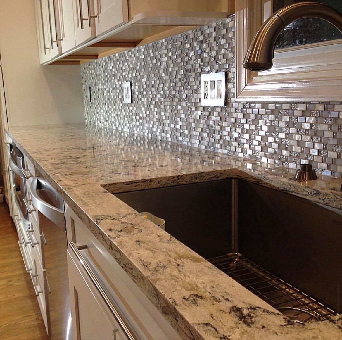 Granite countertop with a mosaic tile backsplash, sink, and cabinets in a kitchen.