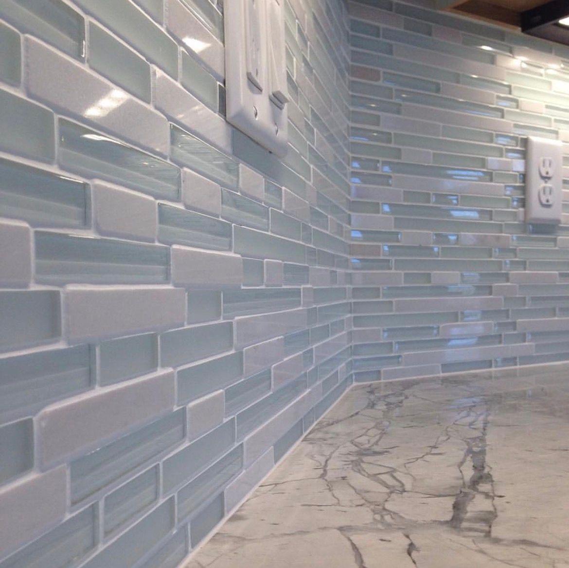 Light blue and white glass tile backsplash in a kitchen with marble countertop.