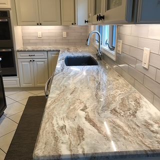 Kitchen counter with granite surface, sink, cabinets, and tile backsplash.