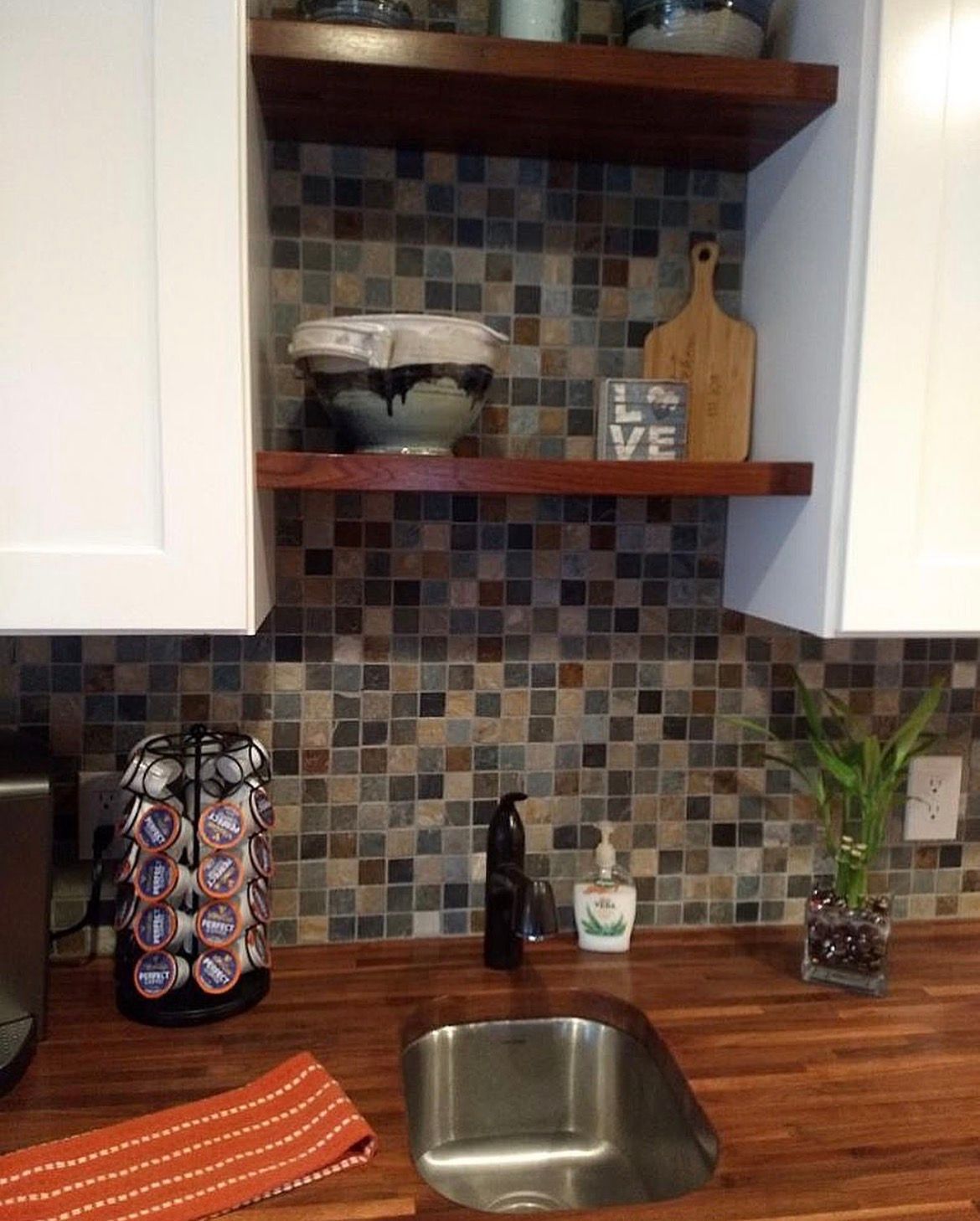 Kitchen nook with wood shelves, tile backsplash, and stainless steel sink.
