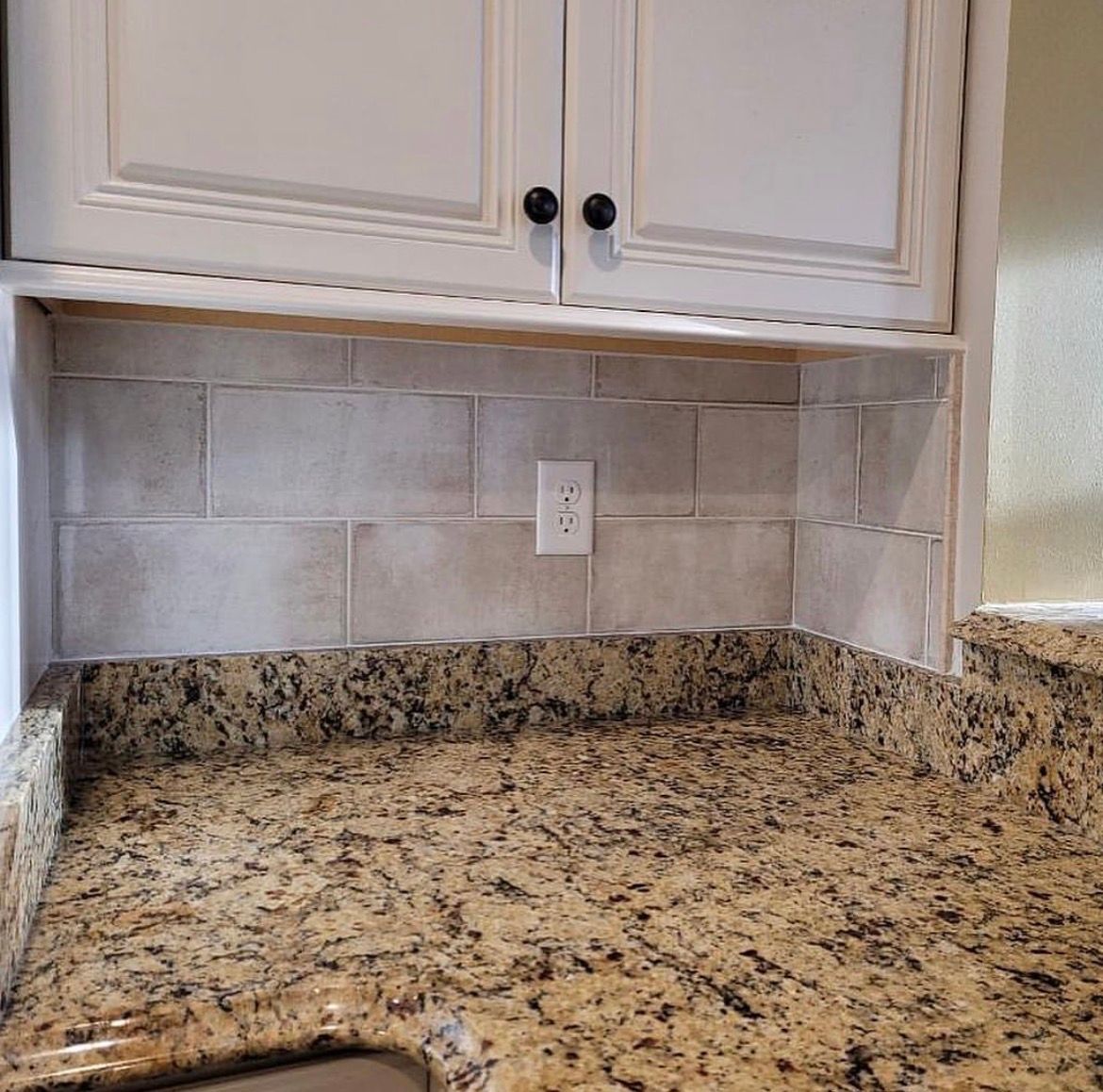 Kitchen with light-colored cabinets, tan tile backsplash, granite countertop, and a power outlet.