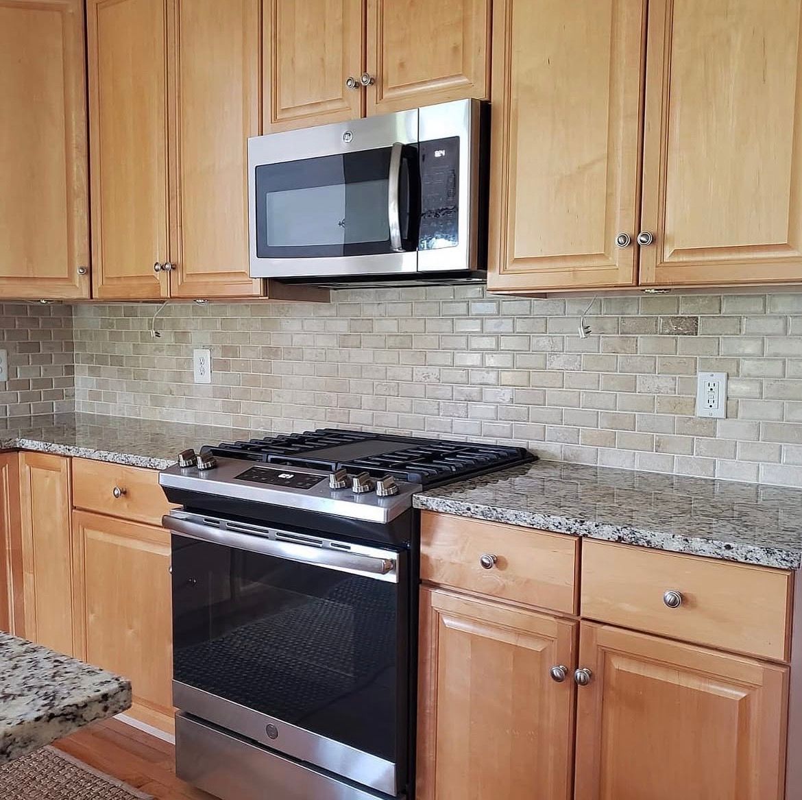 Kitchen with light wood cabinets, stainless steel appliances, and stone backsplash.
