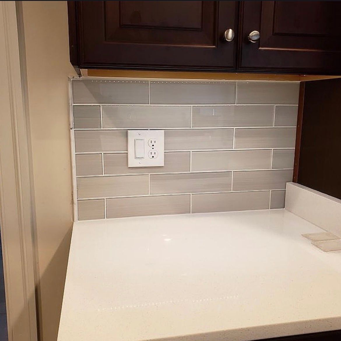 Kitchen with grey subway tile backsplash, white countertop, and dark brown cabinets.