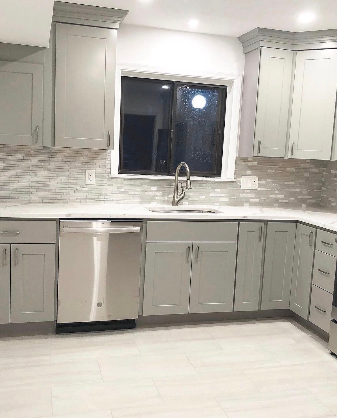 A modern kitchen with gray cabinets, stainless steel appliances, and a window above the sink.