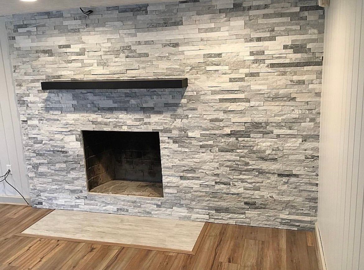 Fireplace with gray stone facade, black mantel, and wood flooring.