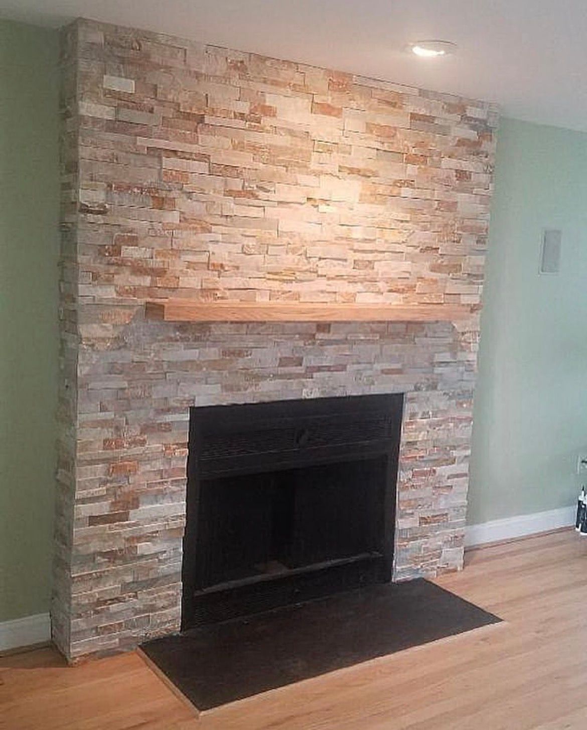 Fireplace with stacked stone surround, wooden mantel, and black hearth.