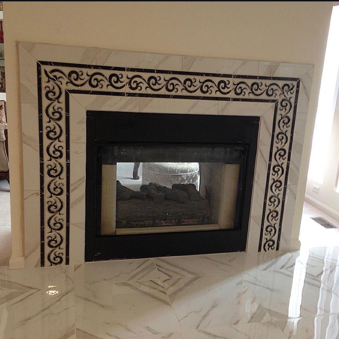 Fireplace with marble surround, black decorative tiles, and reflective glass in a room with marble flooring.