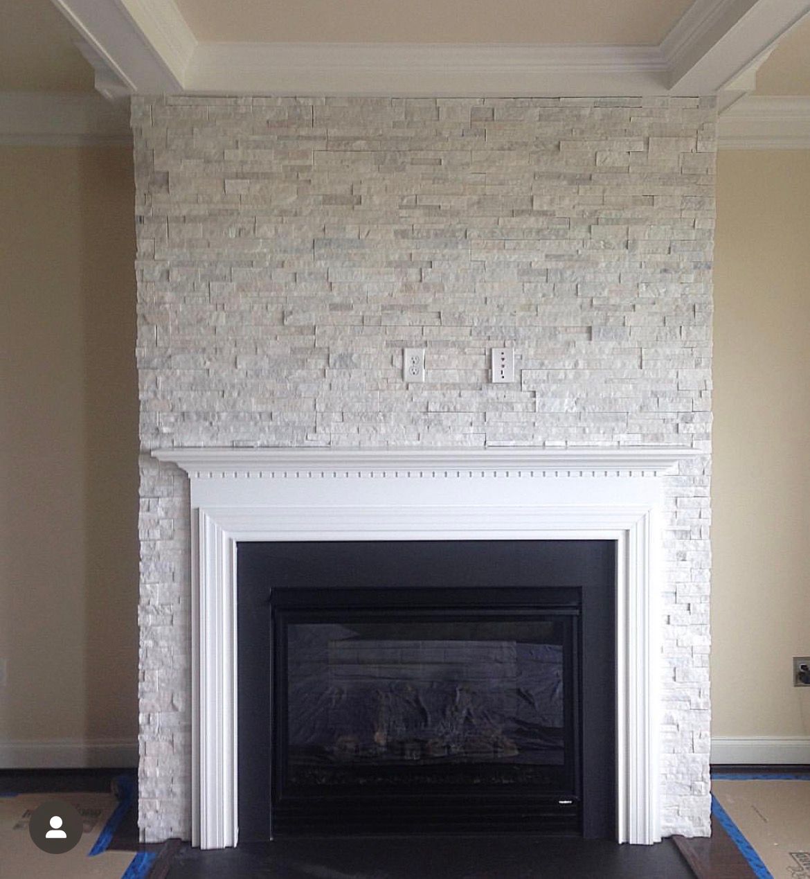 Fireplace with light stone facade and black fireplace insert, white mantel, and tan walls.